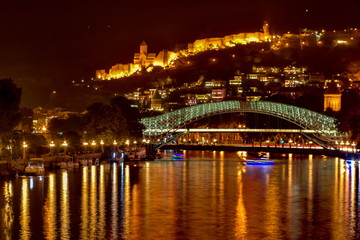 Fototapeta na wymiar Pedestrian Bridge of Peace over the Kura River, Narikala Fortress and Kartlis Deda Monument in Tbilisi, Georgia
