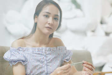 Portrait of young serious beautiful Vietnamese woman in off shoulder blouse holding pen and looking at camera