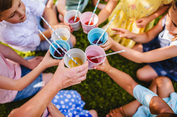 Midsection of small children sitting on ground outdoors in garden in summer, drinking.
