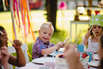Down syndrome child with friends on birthday party outdoors in garden.