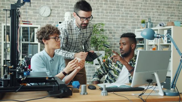 Specialists men and woman are discussing 3d printed shape using computer and 3d printer in office working together as a team. People and teamwork concept.