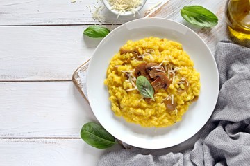 Traditional Italian risotto with mushrooms, saffron and parmesan cheese on white wooden background. Top view with copy space.