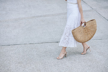 Cropped image of young woman in white lace skirt walking in the street with big straw bag