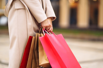 Shopping bags in the hands. Hand of young woman with multi-coloured bags with purchases. Beautiful girl holding shopping bags on the city street. Consumerism, shopping, sales, lifestyle concept. 