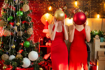 Two sexy hot girls in red dresses hide their faces with Christmas tree decorating balls at...