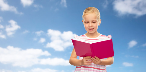 childhood and people concept - smiling little girl reading book over blue sky and clouds background