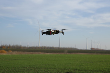 Fototapeta premium quadcopter drone in flight against the background of wind turbines in the field. New technology concept. Agricultural complex