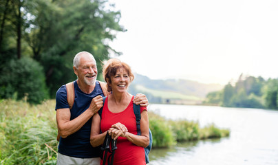 Senior tourist couple on a walk in nature, standing by lake.