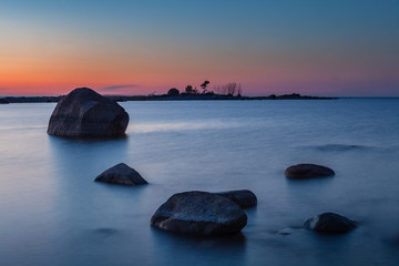 Fototapeta na wymiar Sunset over silhouettes of stones and boulders laying on a shore. Long exposure