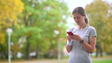 Girl athlete jogging in the evening park. Resting holds a smartphone and listens to music. Workout. Healthy lifestyle. 4k UHD Footage - Powered by Adobe