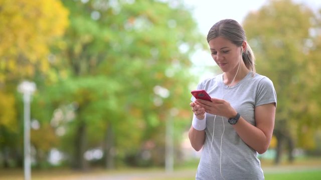 Girl athlete jogging in the evening park. Resting holds a smartphone and listens to music. Workout. Healthy lifestyle. 4k UHD Footage
