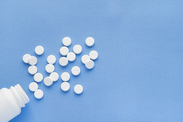 Bottle with white vitamin pills scattered on a blue background.