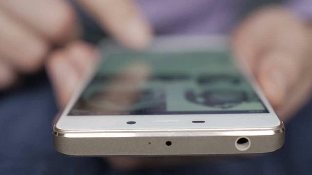 Man using his smartphone with to scroll a Instagram account feed, scrolling news, tapping on screen. The screen is blurred. Focus on the finger. Close-up. 4K UHD.