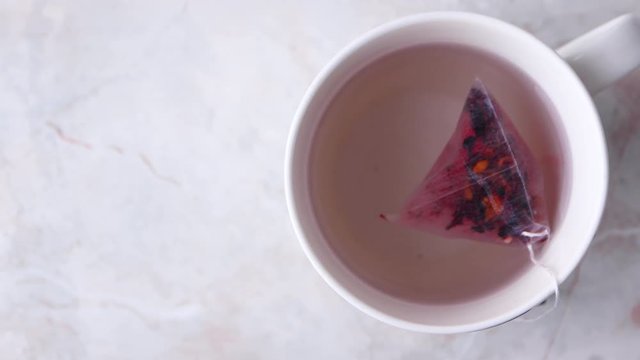 Making fruity tea in tea pyramid bag in white cup on marble background. Cozy winter breakfast mood, top view