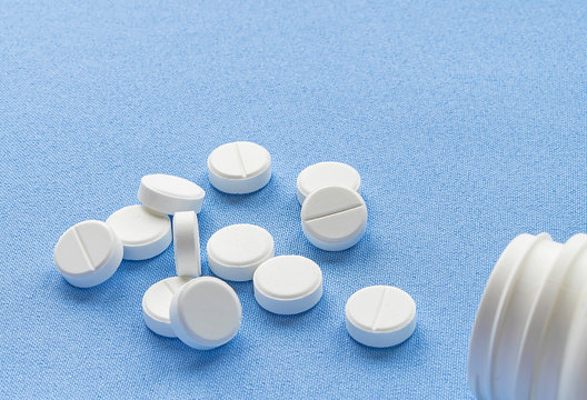 Bottle with white vitamin pills scattered on a blue background.