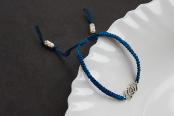 blue braded bracelet with chakra (ajna) on the edge of a snow-white plate