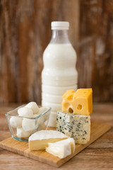food and eating concept - different kinds of cheese and milk on wooden board