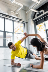 smiling sportsman and sportswoman doing plank and clapping on fitness mats in sports center