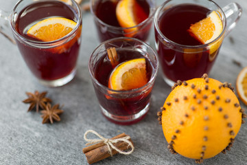 christmas and seasonal drinks concept - glasses of hot mulled wine with orange and cinnamon on grey background