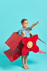 Portrait of smiling excited boy inside of carboard box in form of airplane, imagination of pilot. isolated blue background, sky