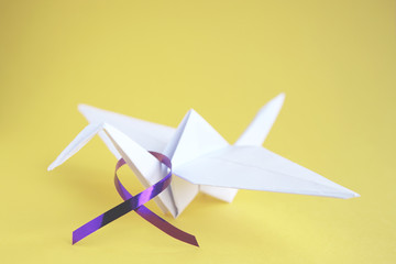   White paper crane with purple ribbon on yellow paper background. Alzheimer's disease, Pancreatic...
