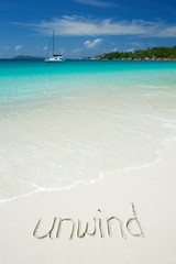 'unwind' message handwritten on smooth sand beach with incoming wave
