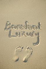 Barefoot Luxury message handwritten in clean sand with pair of footprints
