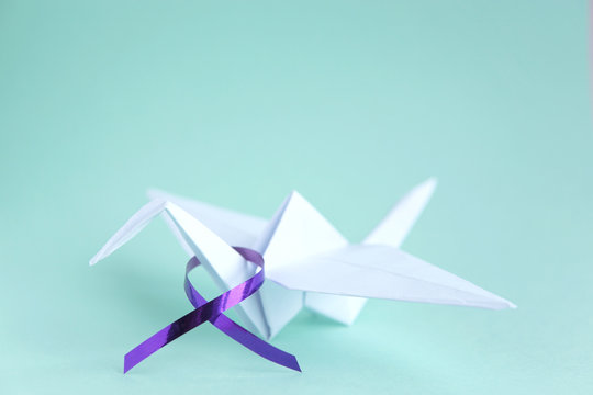  White paper crane with purple ribbon on mint paper background. Alzheimer's disease, Pancreatic cancer, Epilepsy awareness, hope, world cancer day. Hope concept. Copy space. Selective focus.      