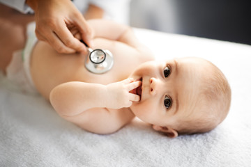 medicine, healthcare and pediatrics concept - close up of female doctor with stethoscope listening to baby girl's patient heartbeat or breath at clinic or hospital