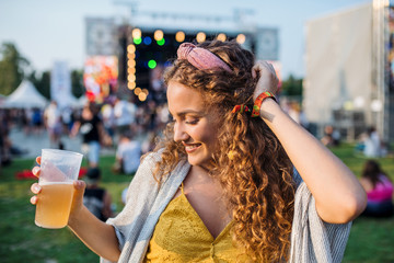 A young woman with drink dancing at summer festival.