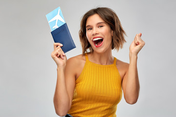 travel, tourism and vacation concept - happy laughing young woman in mustard yellow top with air ticket and passport over grey background