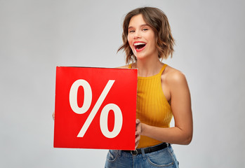 shopping, consumerism and people concept - happy smiling young woman in mustard yellow top and jeans with sale signs over grey background