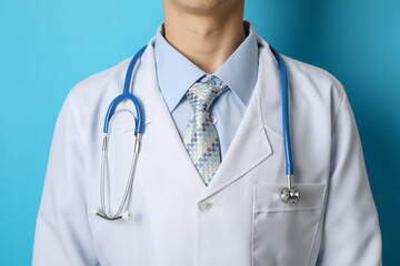 Doctor in medical gown with stethoscope against blue background, close up