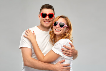 summer accessory, valentines day and love concept - portrait of happy couple in white t-shirts and heart shaped sunglasses over grey background