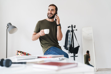 Image of caucasian laughing man talking on cellphone and drinking coffee