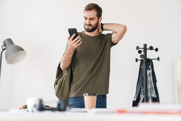 Image of handsome displeased man holding and looking at cellphone