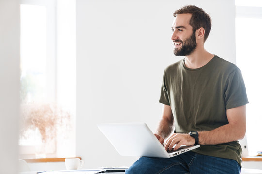 Image of handsome pleased man typing on laptop and laughing