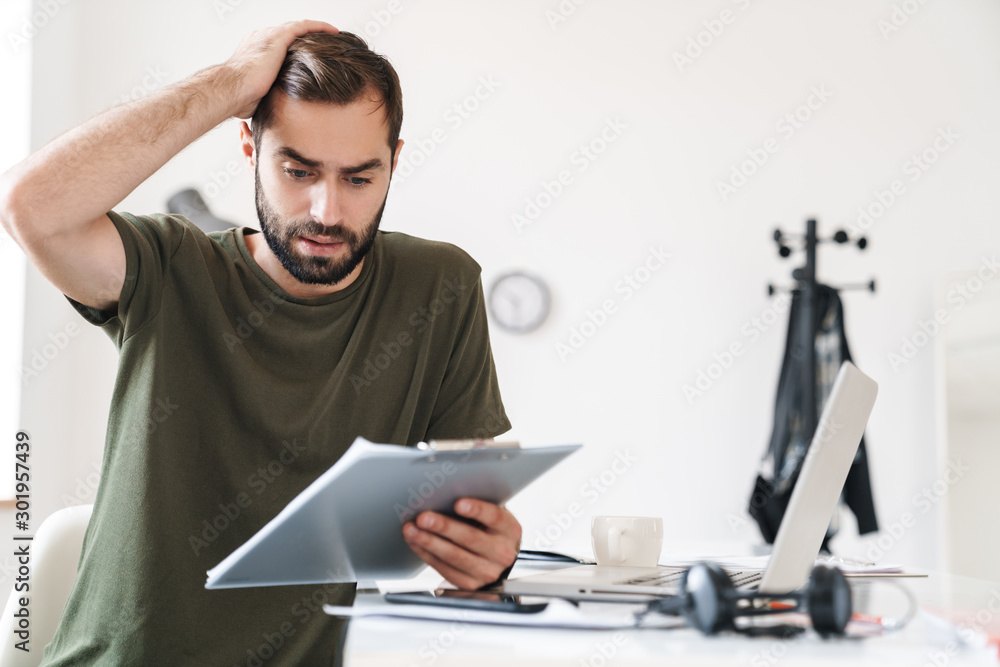 Canvas Prints Image of perplexed handsome man reading documents and holding clipboard