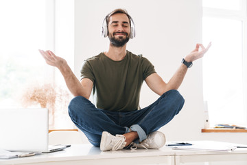 Image of pleased man listening music with headphones while sitting