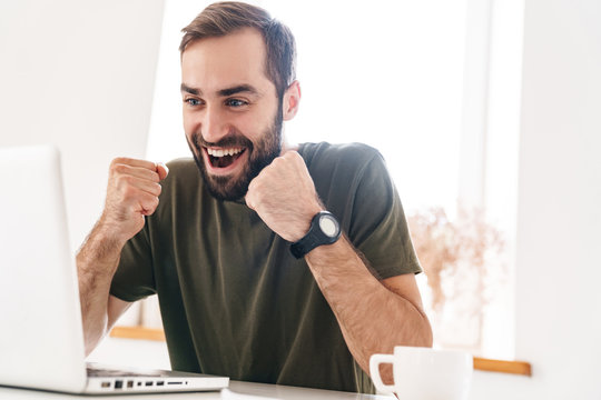 Image of caucasian excited man looking at laptop and drinking coffee