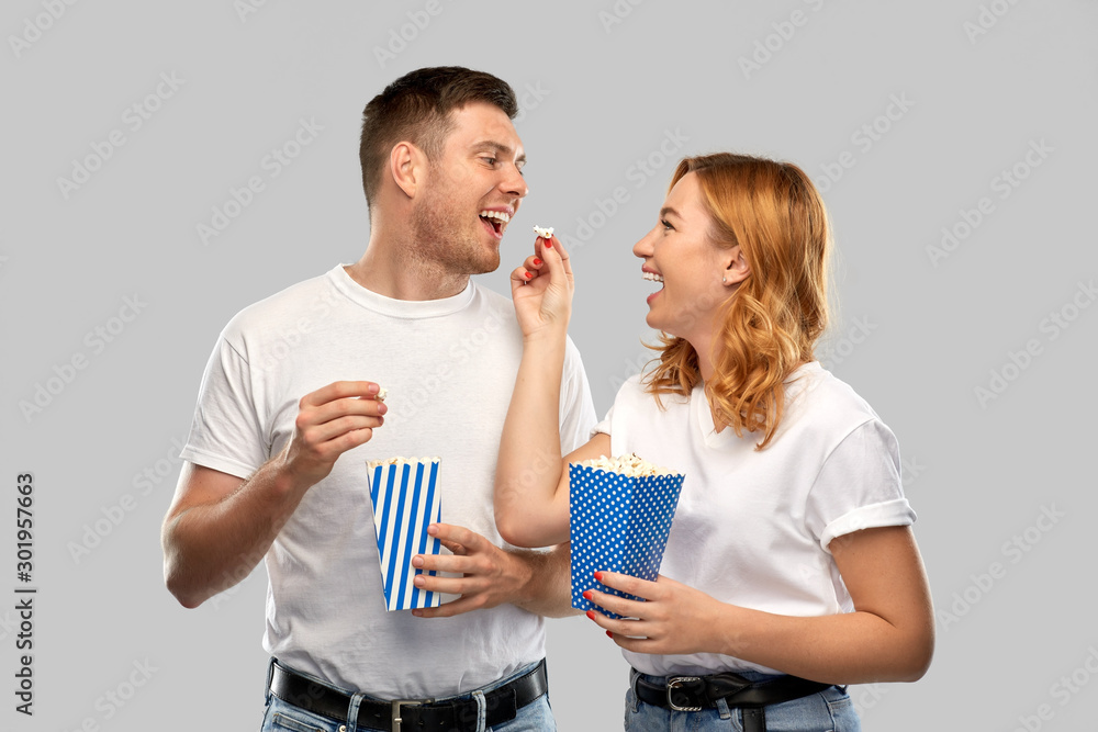 Poster food, entertainment and people concept - portrait of happy couple in white t-shirts eating popcorn over grey background