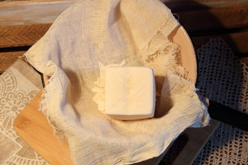 Homemade cheese in cheesecloth on wooden background in rustic style