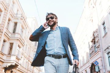 Handsome manager with stubble walking on the street with bag and talking on mobile phone