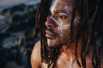 Fototapeta na wymiar Outdoor emotional Fashion Portrait of African man wearing long dreadlocks and fancy makeup white face paint
