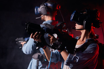 Caucasian man and woman stand holding virtual guns and wearing goggles, in casuan clothes. innovation future, fiction, vr © alfa27