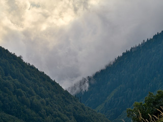 Foggy gorge; dense clouds floating between mountain ranges; trekking route in nature terrain; mountain trail through mist, sunset time in mountain ravine, Bzerpinskiy karniz, Russia