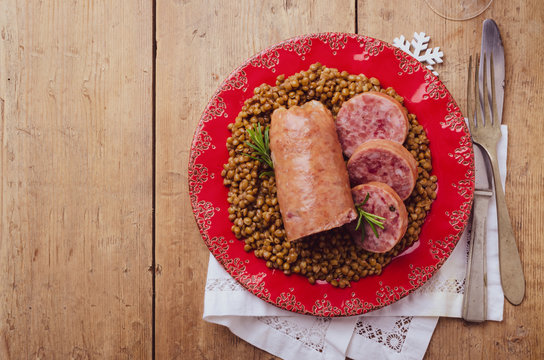 Italian large pork sausage cotechino served  with lentils with rosemary on a  rustic plate.