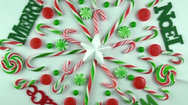 Christmas day traditional Winter Holidays candy cane ornament with cinnamon, peppermint lollipop sweets arranged on white table. Decorated as snowflake with words joy, noel, peace, merry, wish.