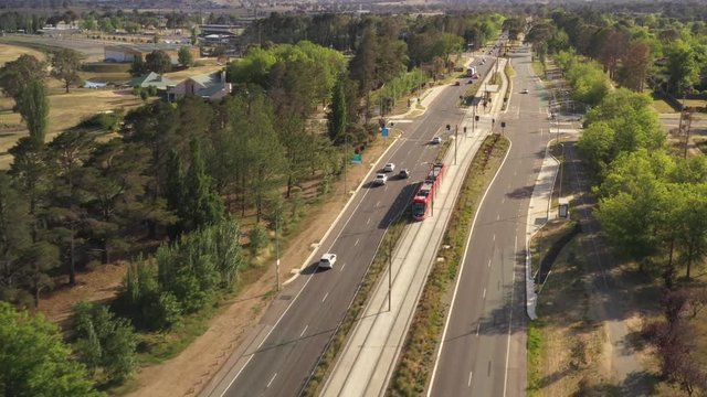 Aerial drone view of a Canberra light rail tram travelling along the Federal Highway to a stop during one of its commutes from Canberra city to Gungahlin in the early morning on a sunny day