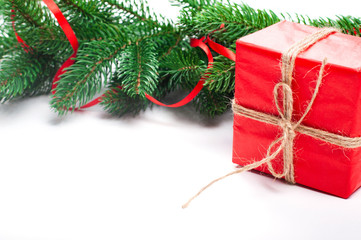 Holiday frame with Christmas tree branches and decorations with small red gift box and red stripe on white wooden background.  Christmas background template for greetin0g cards and social media.